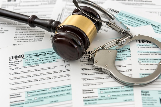 Wooden gavel with handcuff lying on tax form