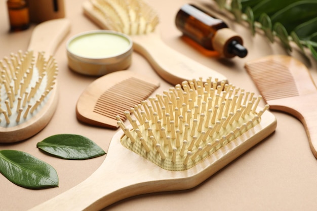 wooden hair brushes combs cosmetic products and green leaves on dark beige background closeup