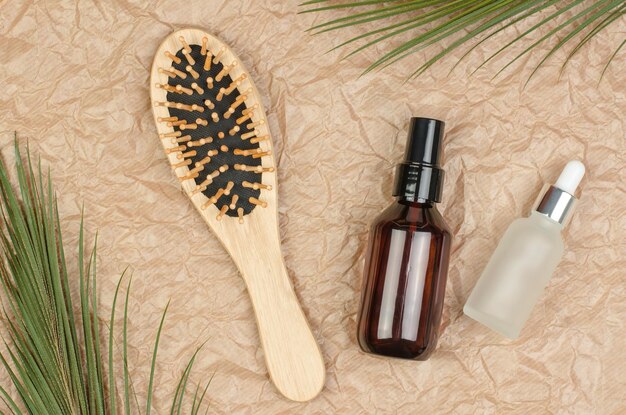 Wooden hairbrush and bottles with oil and serum on the background of crumpled beige parchment paper