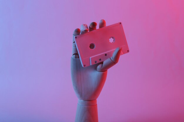 Wooden hand holding audio cassette in pink blue gradient neon light