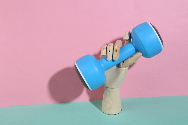 Wooden hand holding dumbbells on blue pink pastel background Trendy shadow Concept art Minimalism Creative layout