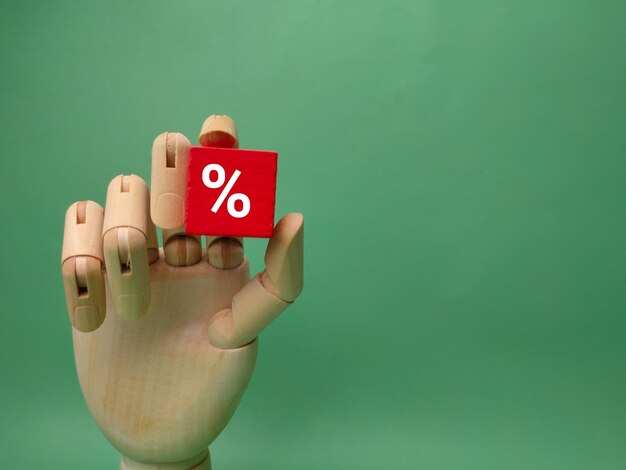 Wooden hand holding red cube with percent icon on a green background Business concept