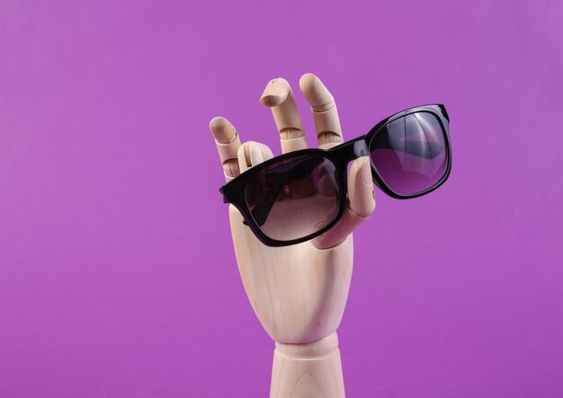 Wooden hand holding sunglasses on purple background