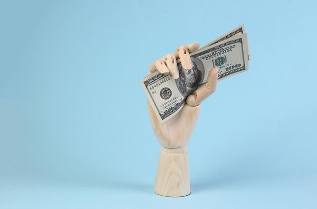 Wooden hand holds dollar bills on blue background