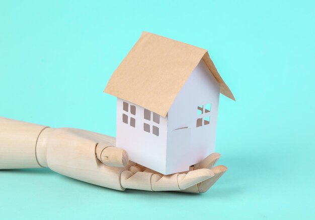 Wooden hand holds house figure on blue background