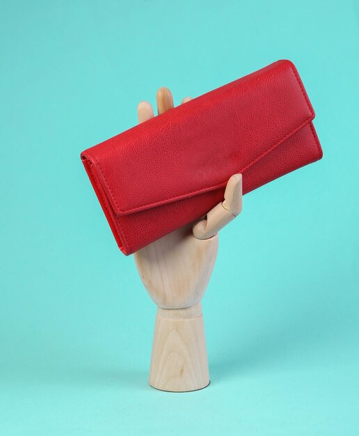 Wooden hand holds red leather wallet on blue background