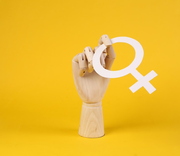 Wooden hand holds venus symbol on yellow background