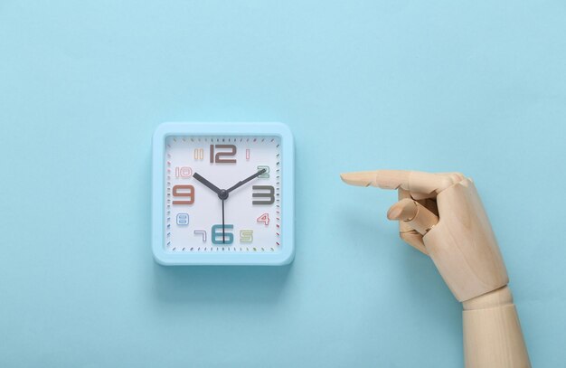 Wooden hand points to an alarm clock on blue background