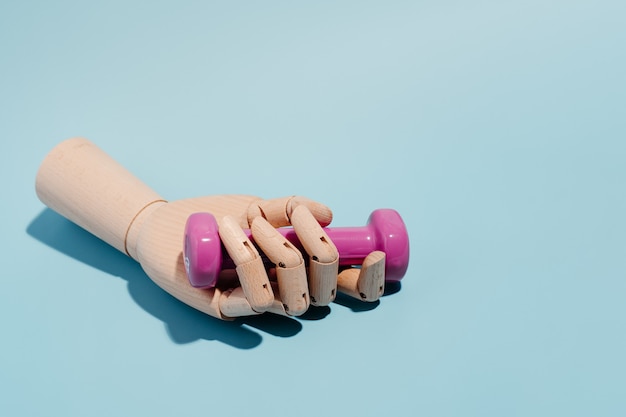 Photo wooden hand with a pink dumbbell on blue background. sport and exercise. 3d illustration