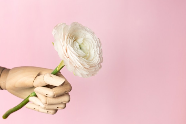 Wooden hand with a white flower on a pink