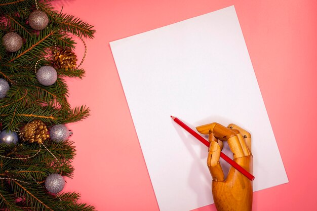 Wooden hand writes Christmas letter to Santa on white paper on pink background..