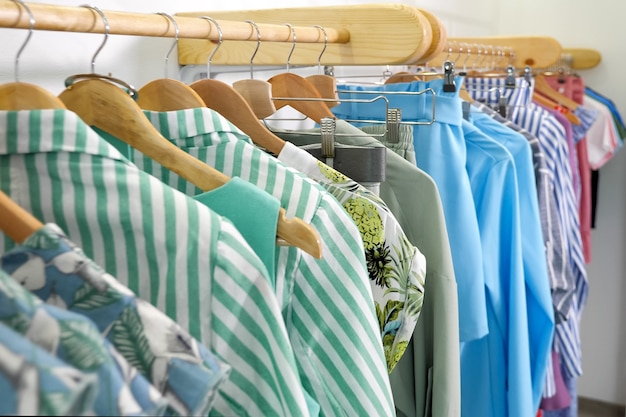 Wooden hangers with fashionable colorful summer clothes on rack in modern designer shop closeup