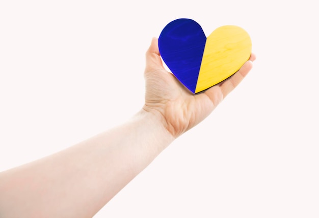 The wooden heart in colors of Ukrainian flag in woman's hands