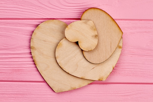 Wooden hearts on pink wooden background. Different sizes plywood hearts on colorful textured wood.