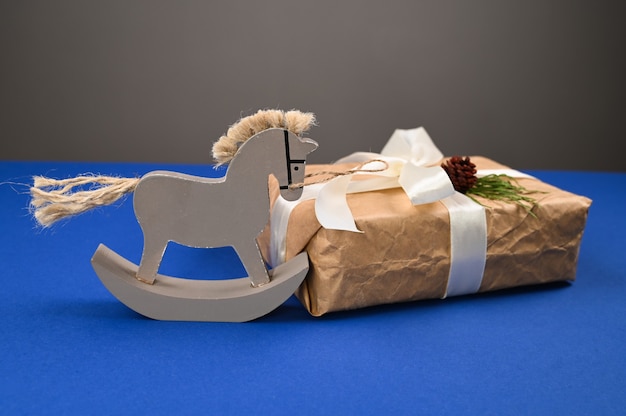 Деревянная лошадь с подарочной упаковкой на синем фоне. Фото высокого качества