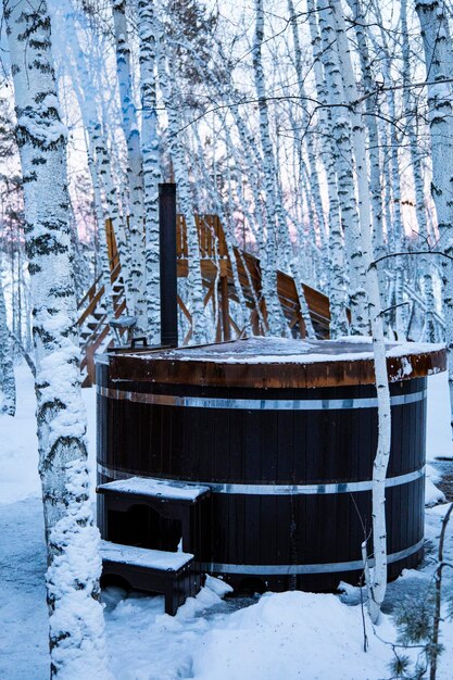 Una vasca calda di legno è seduta nel mezzo di una foresta innevata