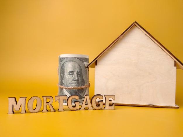 Wooden house and banknotes with word MORTGAGE on yellow background