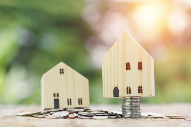 Wooden house on coins stacked blur nature background, saving for future, property investment, business concept.