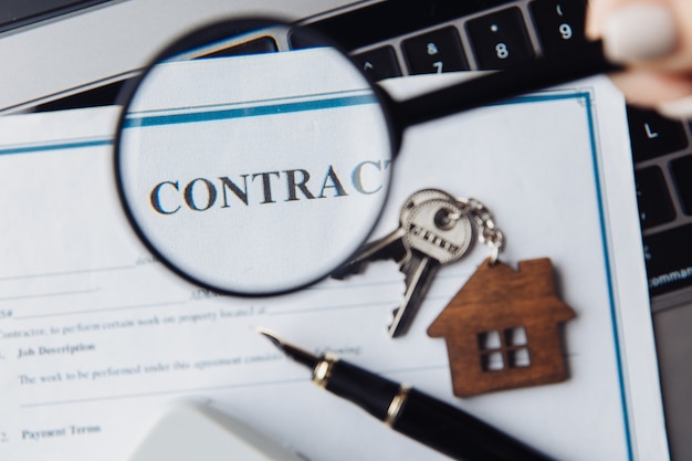 Wooden house, magnifying glass and contract 