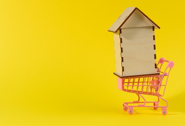 Wooden house in a metal miniature cart on a yellow surface. Real estate purchase concept, mortgage,copy space