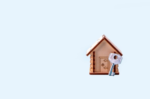 Wooden house model and key on blue background. Concept of buying and selling homes and real estate. Home Insurance, property and mortgage. Copy space for text.