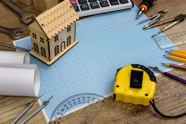 Wooden house model on millimeter paper with different tools