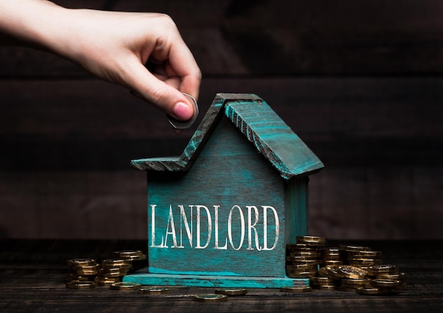 Wooden house model with coins next to it and hand