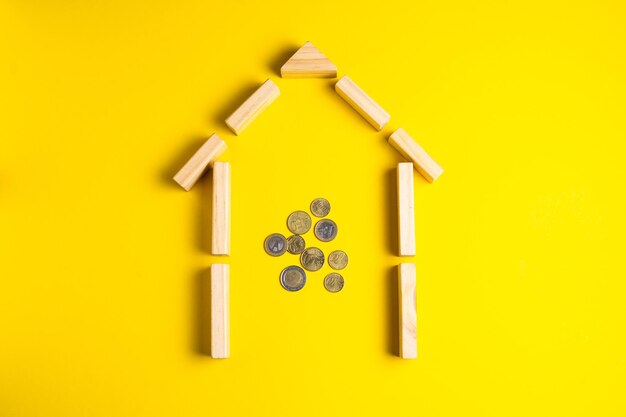 Wooden house model with coins money copy space on yellow background