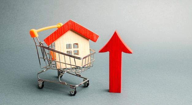 Photo wooden house in a supermarket trolley and red arrow up