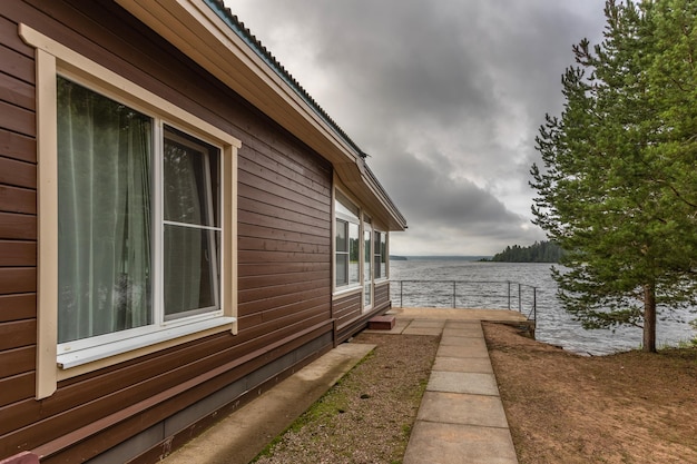 Wooden house with a green tree on the lake in cloudy weather with clouds in the sky