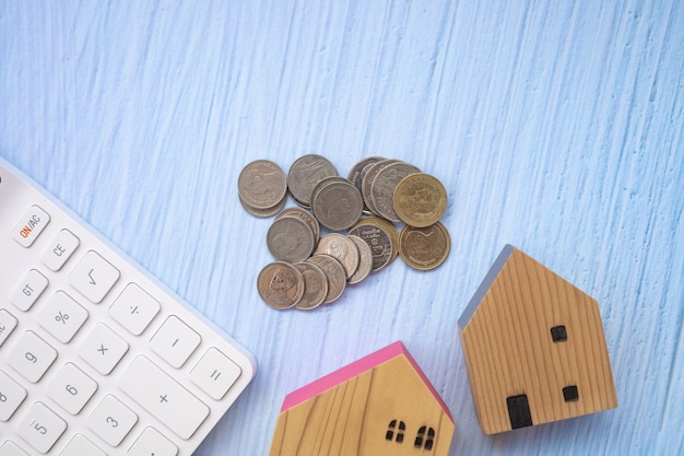 Wooden houses, coins and a white keyboard on a blue wooden background