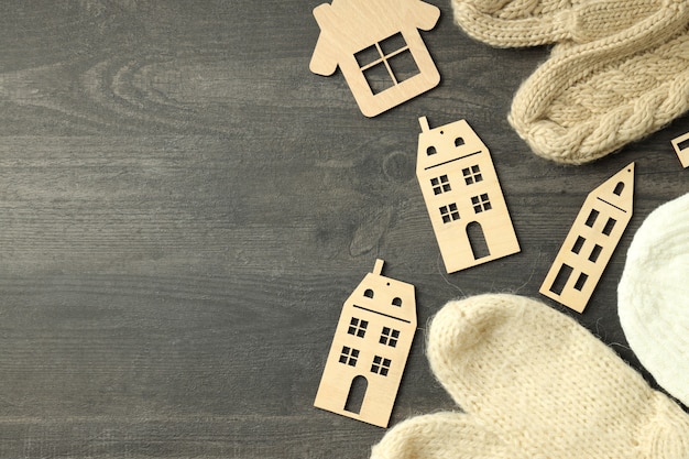 Wooden houses and knitted clothes on gray wooden table.