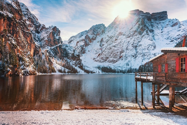 Case di legno nella neve sullo sfondo delle acque cristalline del lago di braies nelle dolomiti, italia. paesaggio invernale colorato nelle alpi italiane innevate, una popolare meta turistica in italia