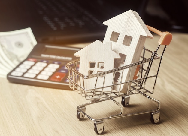 Wooden houses in a supermarket trolley, money and a calculator. Real Estate Market Analytics. 