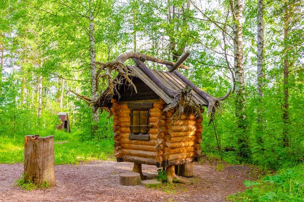 A wooden hut in the woods with a tree branch on the top.