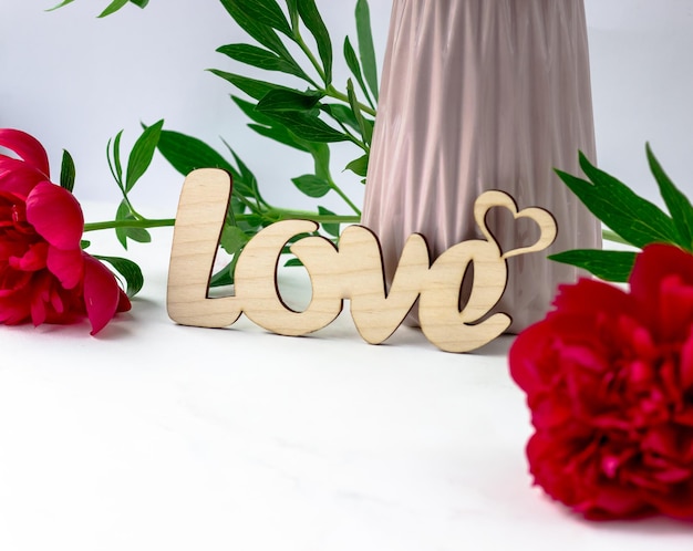 Wooden inscription love on a background of peonies on a white background Postcard with text space