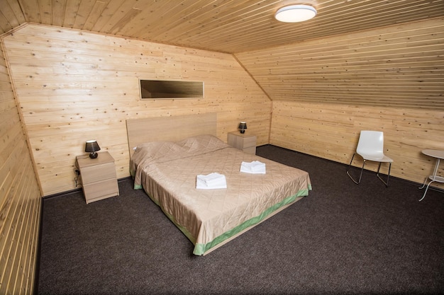 The wooden interior of the hotel suit with double bed with\
beige cover, tables and chairs, flooring roll on the floor;\
accommodation concept.