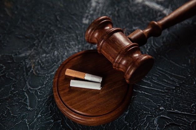 Wooden judge gavel and broken cigarette on grey surface. Tobacco law