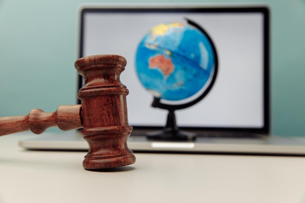 木製の裁判官のガベルのクローズアップとラップトップ上の地球儀。国際法の概念。