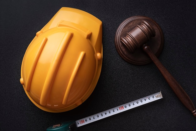 Wooden judge gavel, yellow building helmet and tape. Labor-related legal concept. Top view.