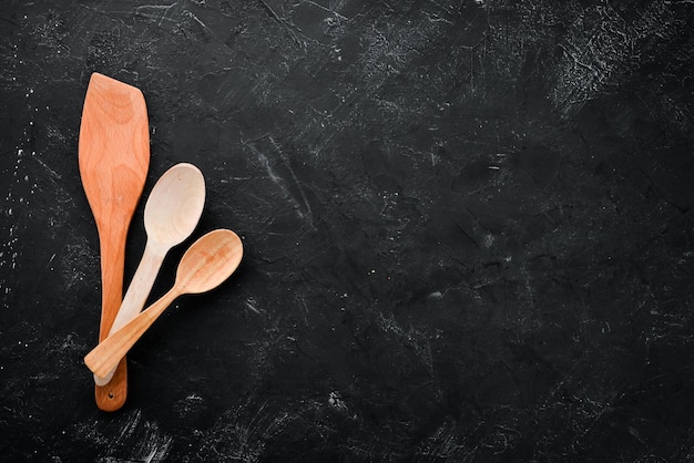 Wooden kitchen utensils On a black stone background Top view Free copy space