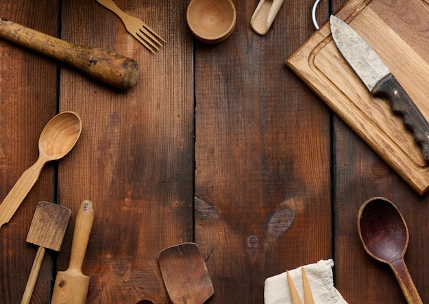 Wooden kitchen vintage items: knife, rolling pin, empty spoons on brown wooden table, top view. Copy space