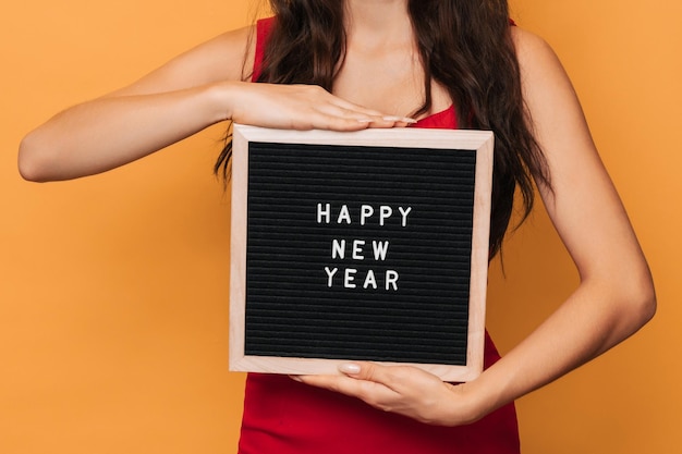 黄色の背景に分離された、新年あけましておめでとうございます、その上にプラスチックの文字の碑文と女性の手に木製の文字板。