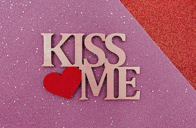 Wooden lettering KISS ME with heart on felt glittering background.