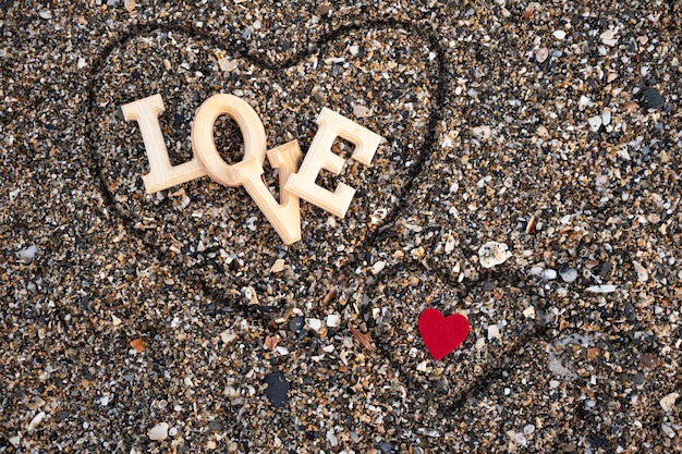 Wooden letters forming the word love with a red heart on beach sand, inside a heart made with the fingers. concept of san valentine