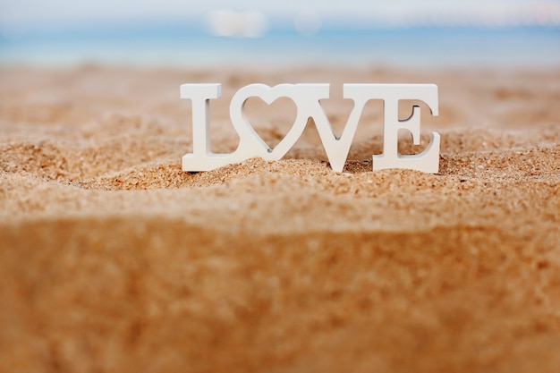 Le lettere di legno amano su una spiaggia sabbiosa che trascura il mare blu