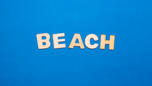 Wooden letters on plain colored background with the word written in English Beach