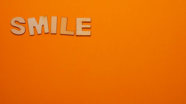 Деревянные буквы на однотонном фоне со словом, написанным на английском Smile