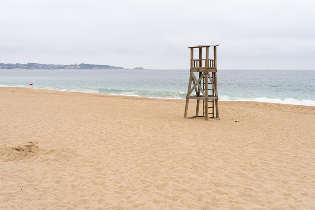 Torre del bagnino in legno fuori servizio sulla spiaggia vuota con bandiera rossa sulla riva ad algarrobo cile