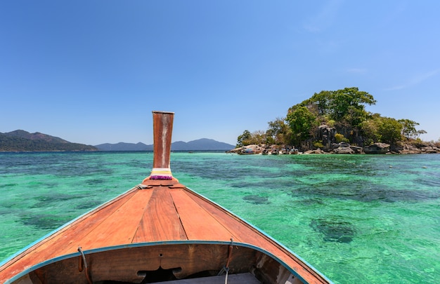 Wooden long-tail boat sailing on emerald sea